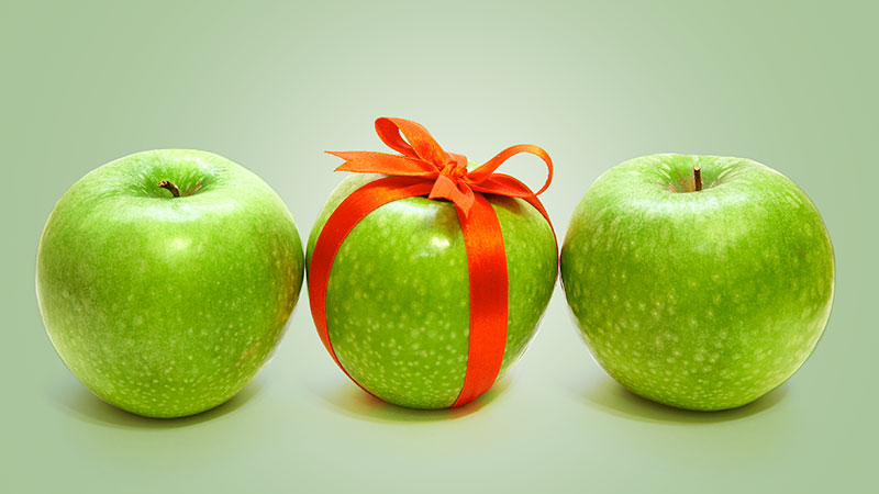 Three green apples with a red bow on the middle apple