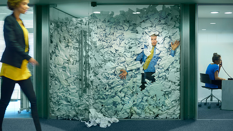 Man Trapped in Glass Office Filled with Crumpled Paper